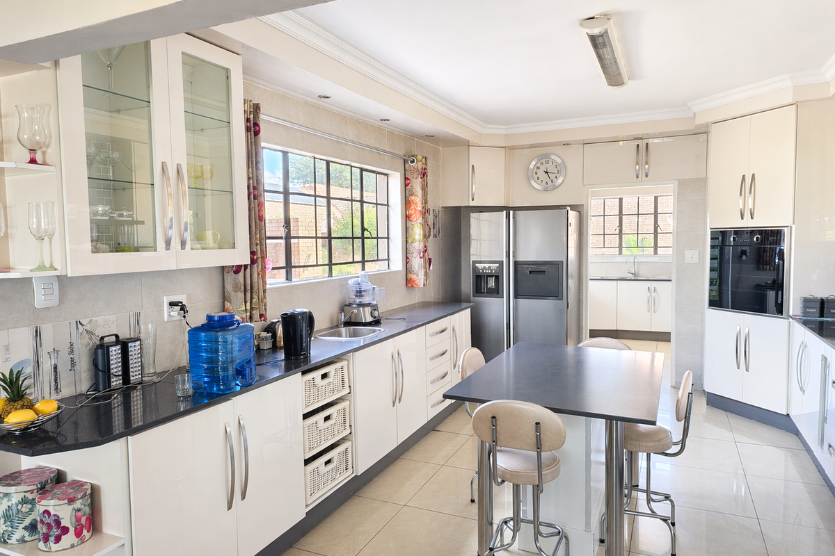 A well-maintained kitchen featuring modern white cabinetry, granite countertops, integrated appliances, and a central breakfast island with tiled flooring.
