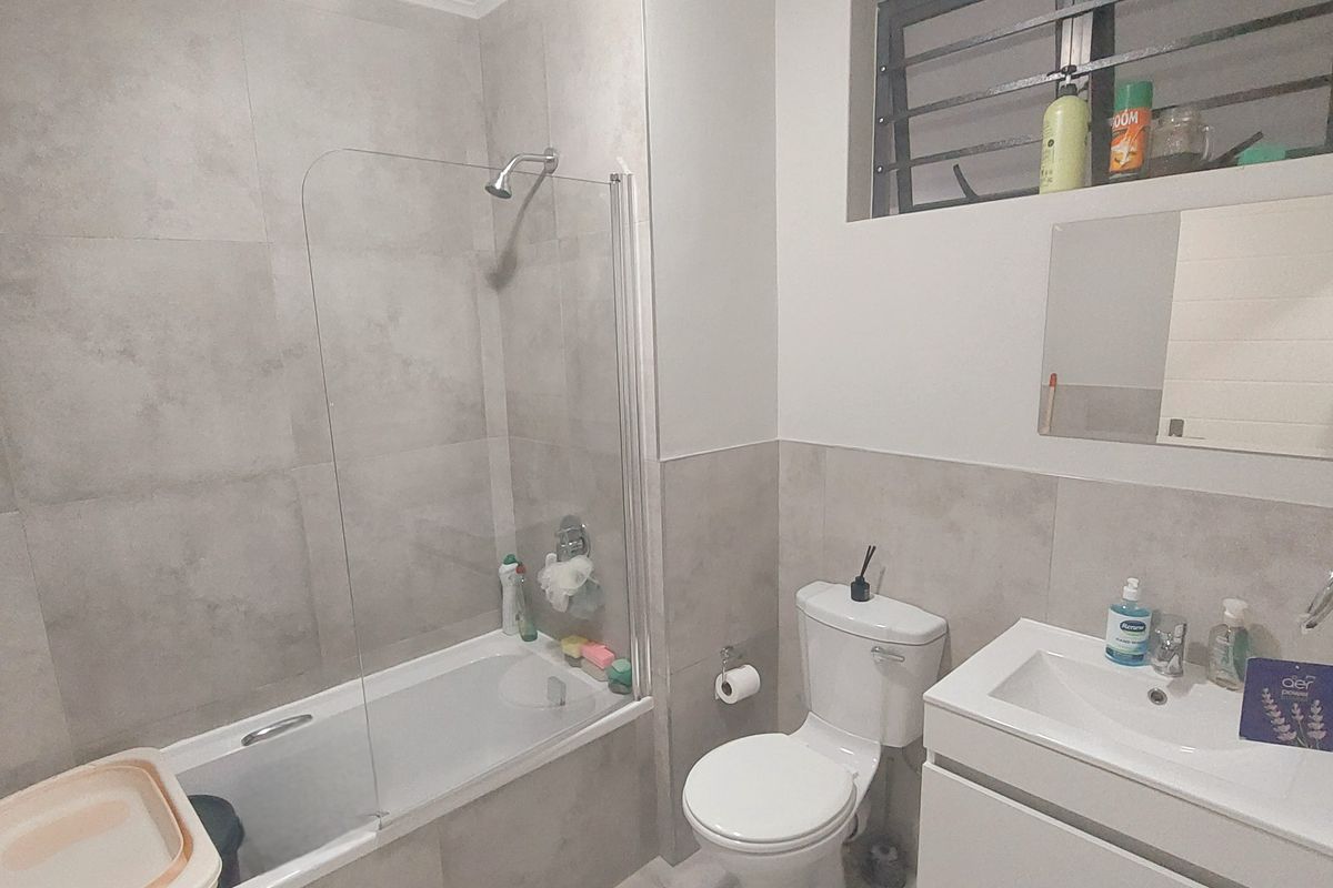 Modern bathroom featuring a bathtub with a glass shower screen, a wall-mounted vanity with a basin, and neutral grey floor-to-ceiling wall tiles.