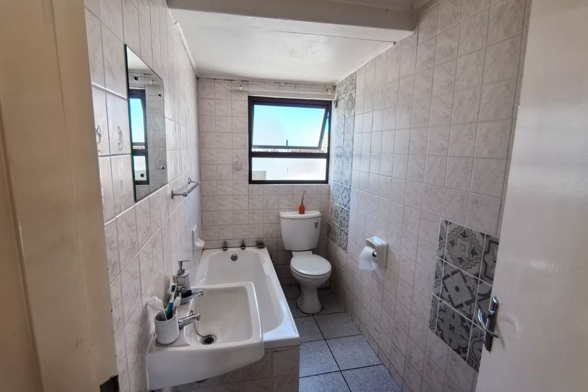 A compact bathroom featuring a bathtub, pedestal basin, and toilet, finished with full-height wall tiling and a window for natural light.