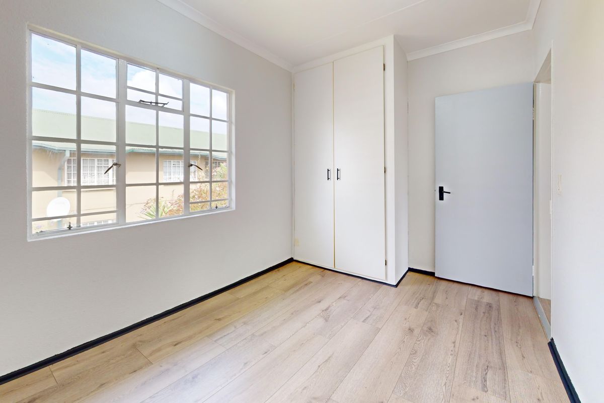 A bright, empty bedroom featuring light-toned laminate flooring, a built-in wardrobe, and a window with classic muntin detailing.