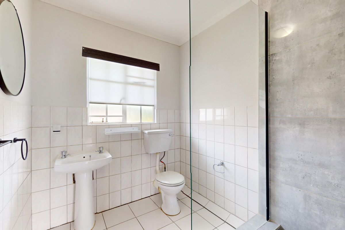 A clean, functional bathroom featuring a pedestal basin, toilet, and a walk-in shower with a glass screen and modern grey wall tiles.