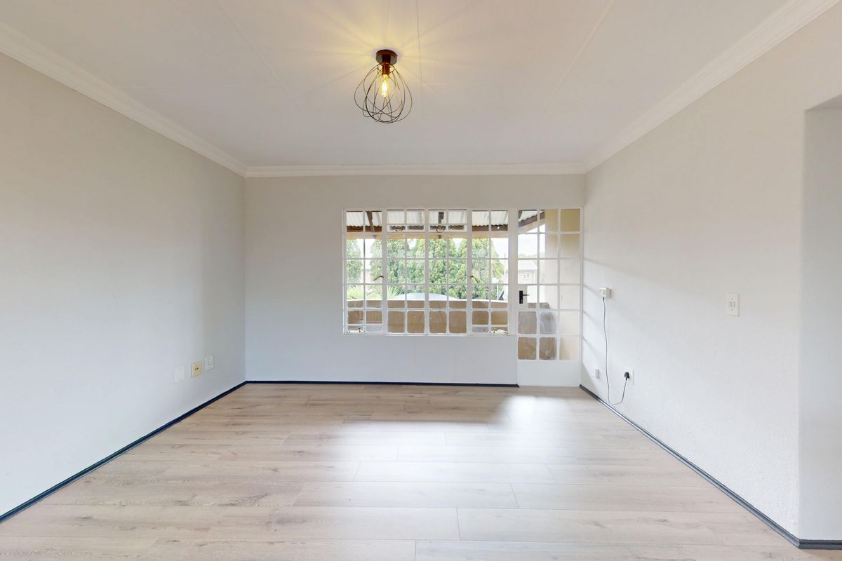 A bright, empty living room featuring modern laminate flooring, crisp white walls, cove cornicing, and a glass-paneled door leading to an outdoor area.