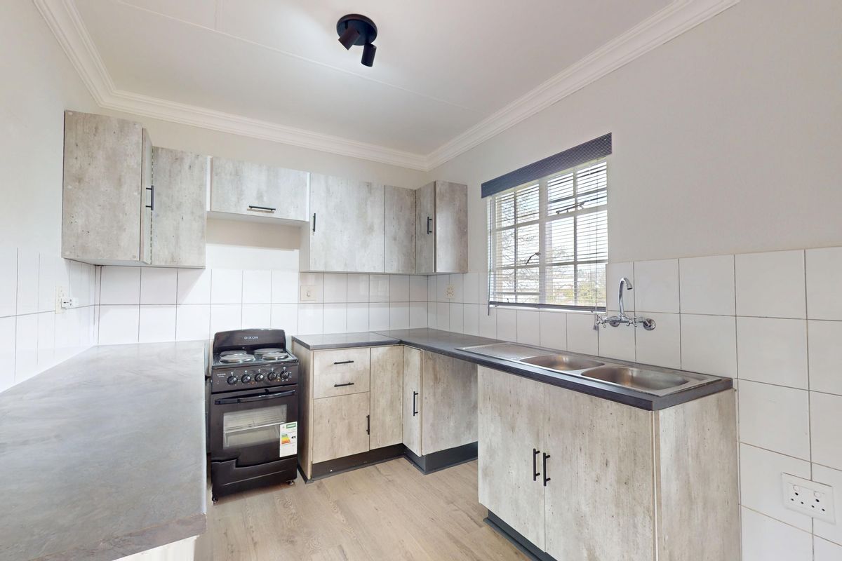 A clean, functional kitchen featuring light wood-look cabinetry, laminate countertops, a double sink, and a freestanding stove with tiled splashbacks.