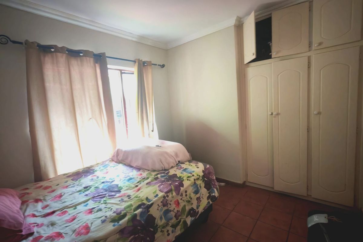 A bedroom featuring built-in cupboards, tiled flooring, and decorative cornicing, offering a functional space with natural light.