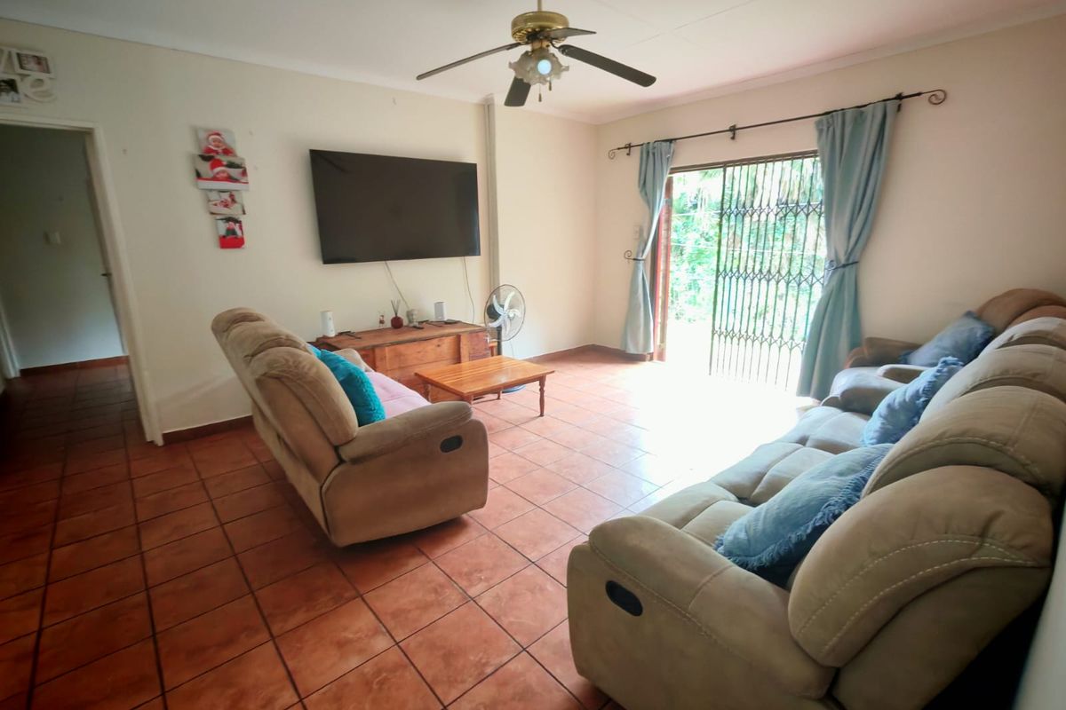 A spacious living room featuring terracotta floor tiles, a ceiling fan, and a sliding door with a security gate leading to the outdoors.