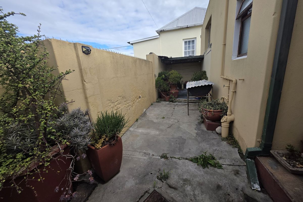 A narrow rear courtyard area featuring concrete paving, boundary walls, and external plumbing fixtures, requiring maintenance and surface repairs.