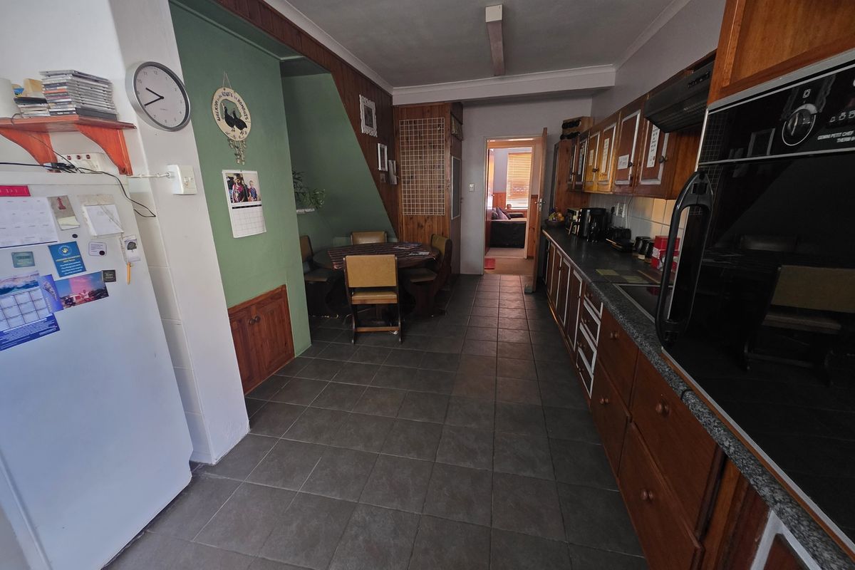 A functional kitchen featuring built-in wooden cabinetry, tiled flooring, and integrated oven, with an adjacent dining area tucked under the staircase.