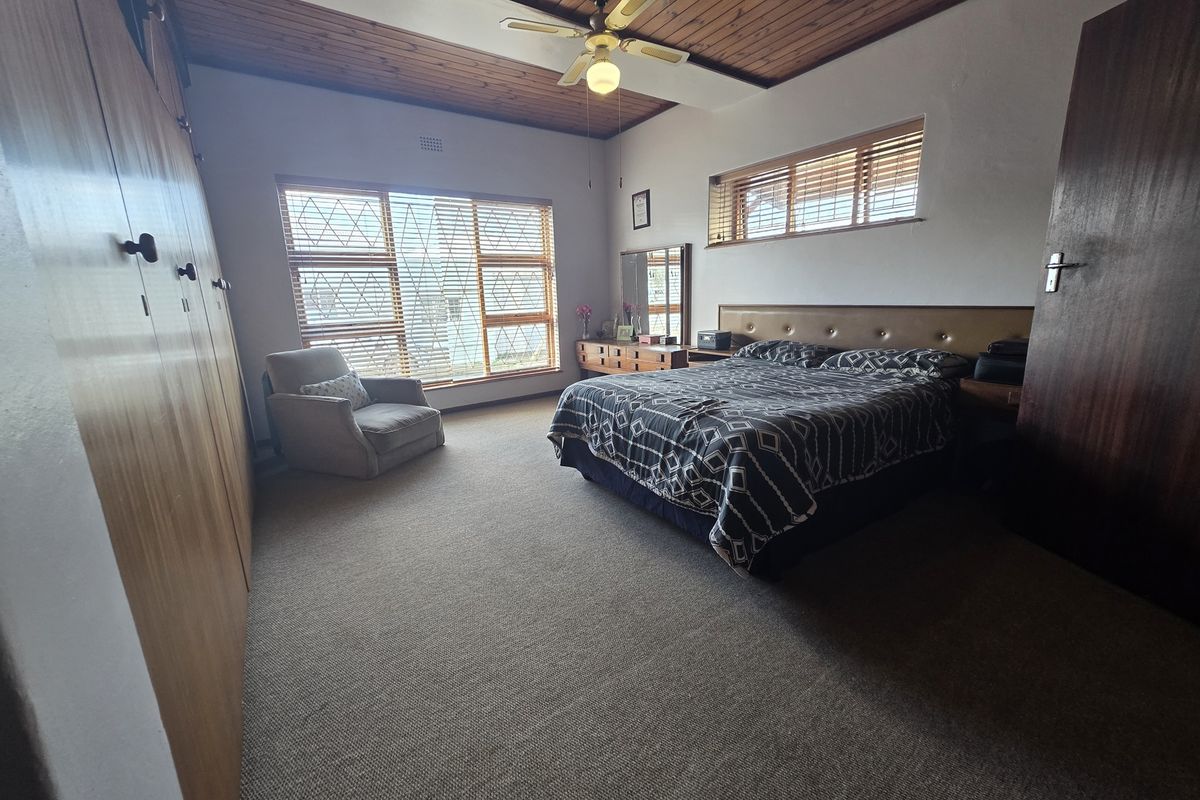 Spacious bedroom featuring built-in cupboards, a timber-paneled ceiling with a fan, and large windows with security bars.