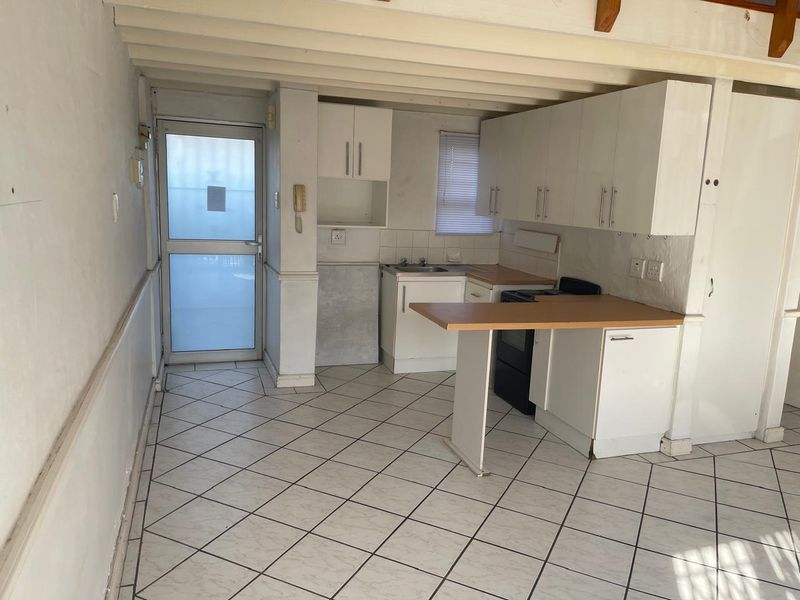 A compact, functional kitchen featuring white cabinetry, laminate countertops, tiled flooring, and exposed ceiling beams, with direct access to an exterior door.