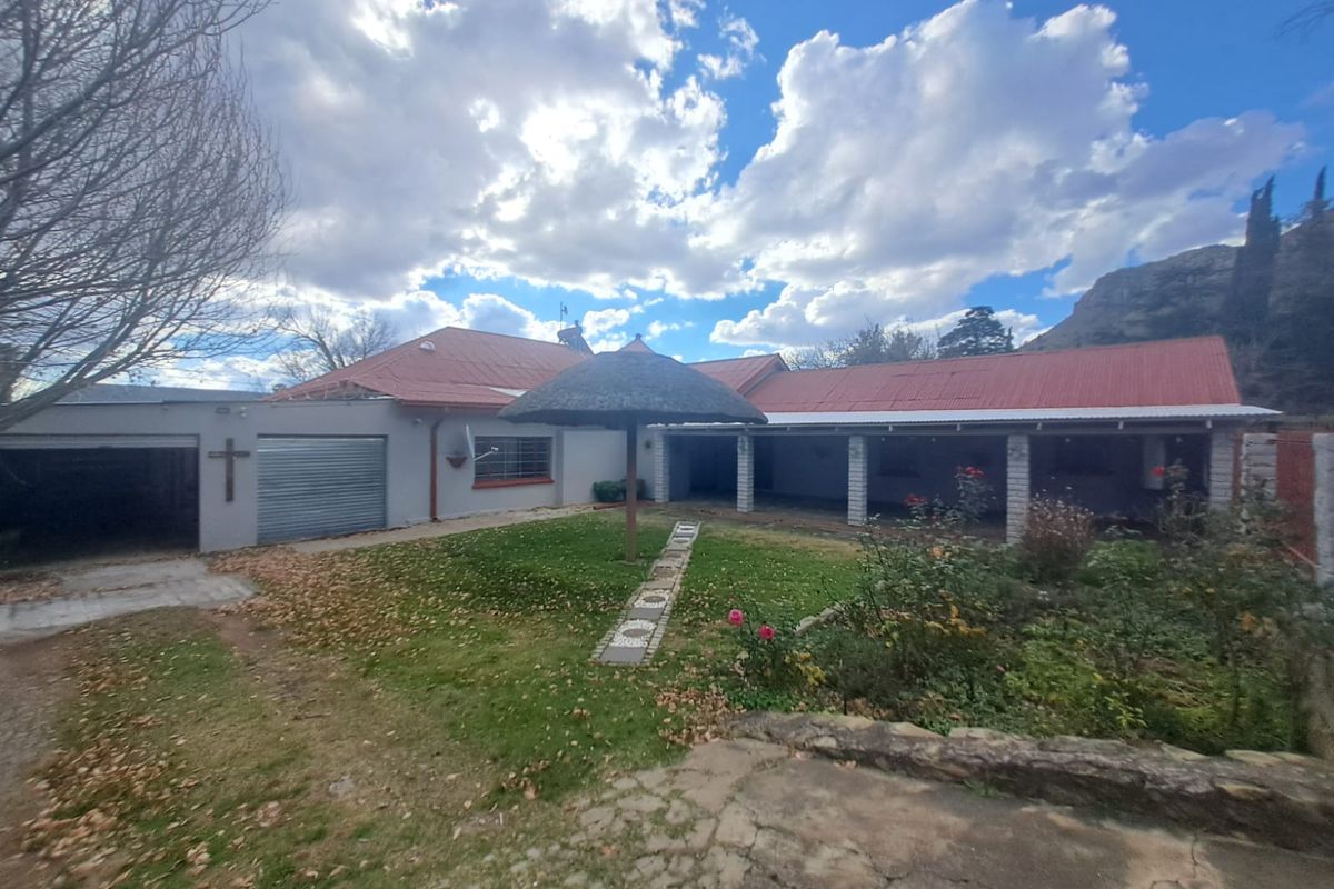 Rear view of the property featuring a covered patio, attached garage with roller door, and a garden area with stone retaining wall.