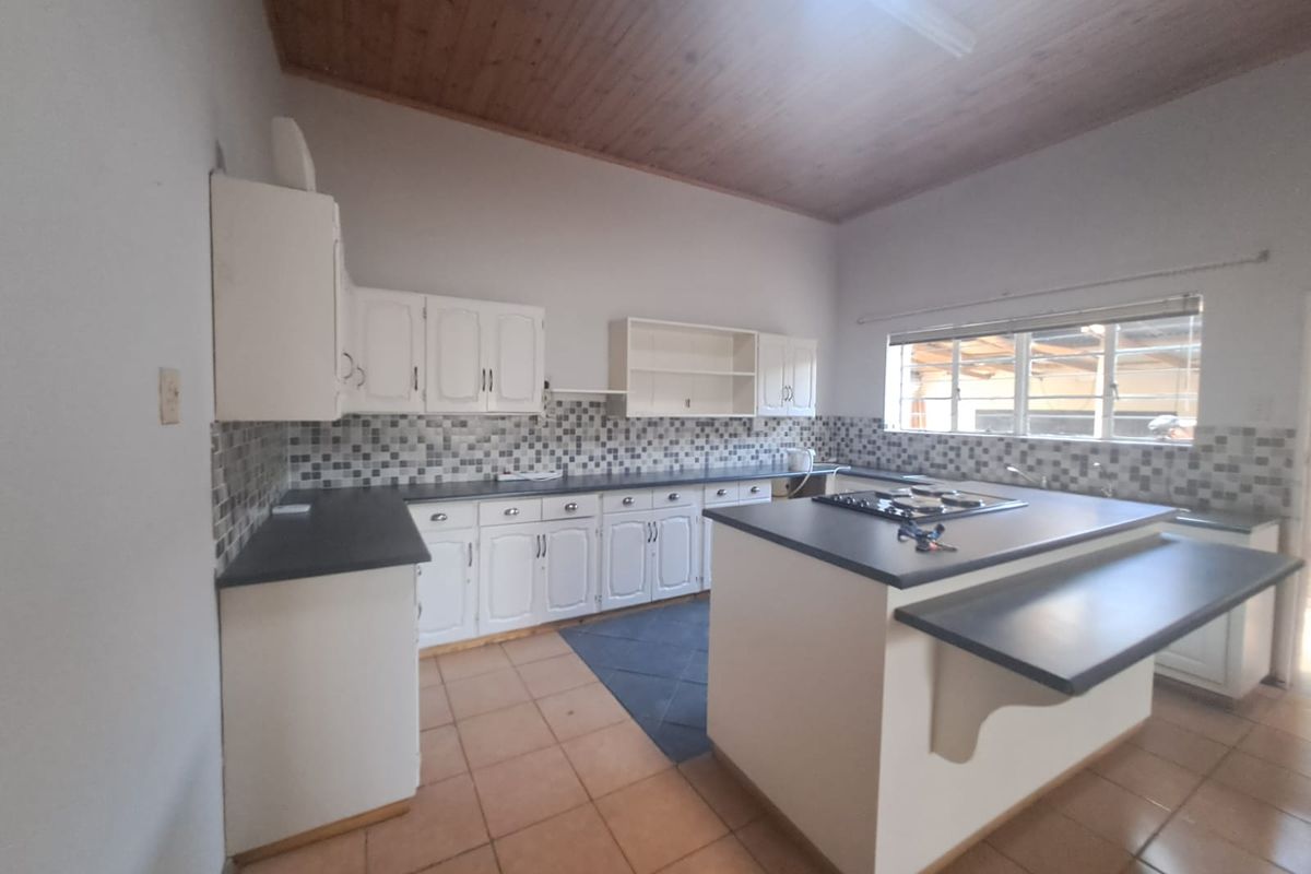 Spacious kitchen featuring a central island with built-in hob, ample cabinetry, tiled backsplash, and a high timber-clad ceiling.