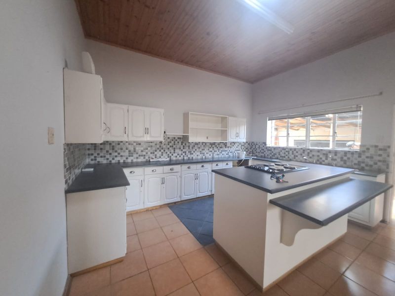 Spacious kitchen featuring a central island with built-in hob, ample cabinetry, tiled backsplash, and a high timber-clad ceiling.