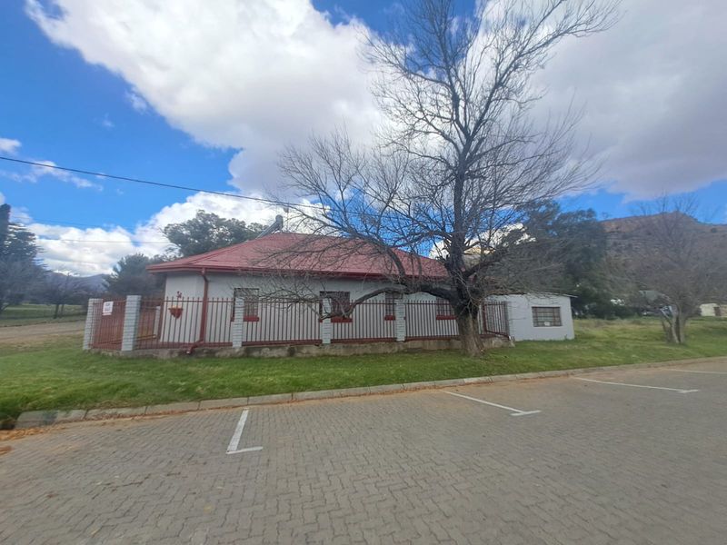 A single-story house with a red metal roof, perimeter fencing, and an adjacent paved parking area, set in a quiet neighborhood.