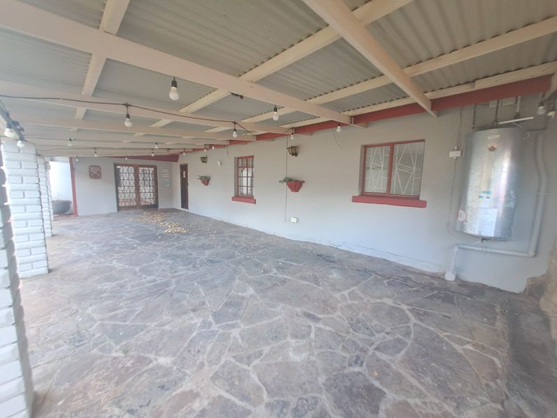 A spacious covered patio featuring stone flooring, exposed timber rafters, and an external geyser, offering a functional outdoor entertainment area.