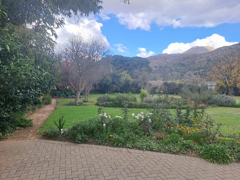 A well-maintained garden featuring a paved walkway, lush lawn, established flower beds, and scenic mountain views.