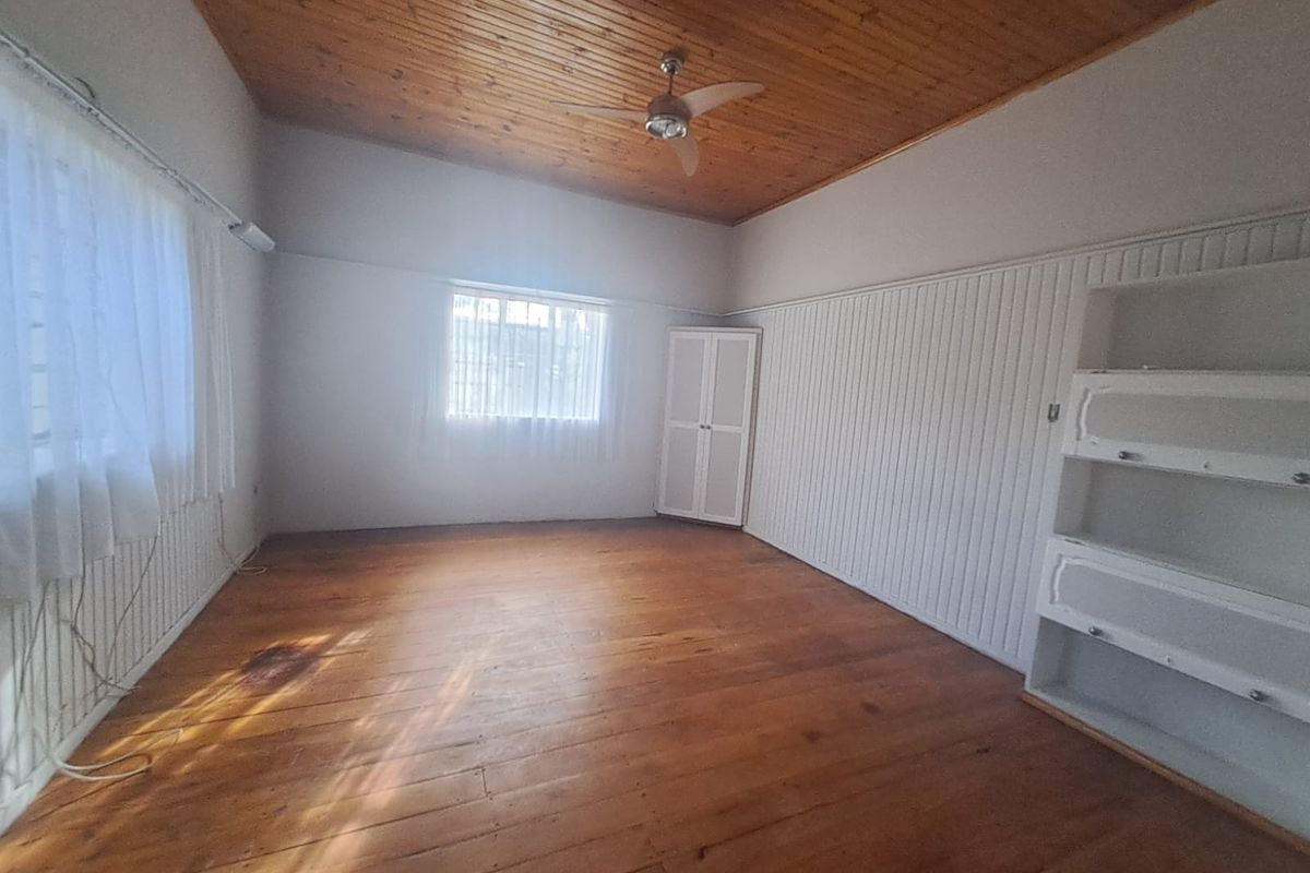 Spacious bedroom featuring original timber flooring, a warm timber ceiling, built-in shelving, and classic vertical wall paneling.