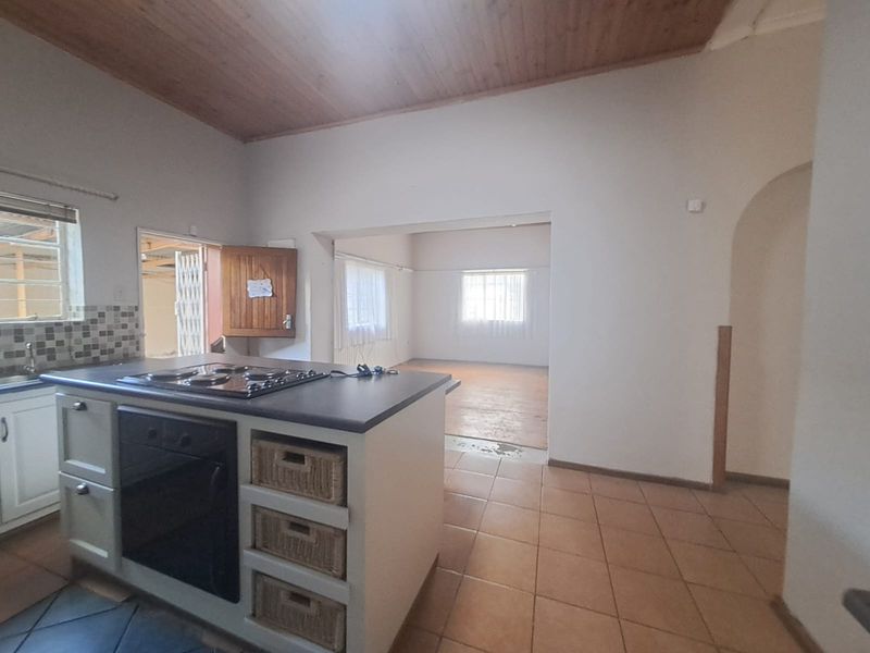 Open plan kitchen and living area featuring a central island with built-in oven and hob, timber ceiling, and tiled flooring throughout.