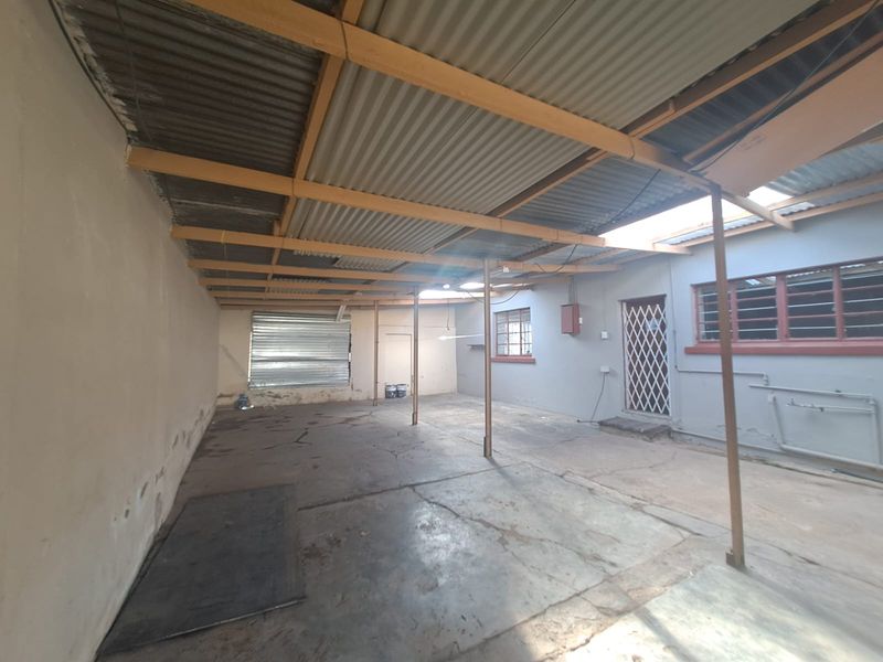 A large, covered outdoor patio area featuring concrete flooring, steel support columns, and a corrugated metal roof, offering a blank canvas for renovation.