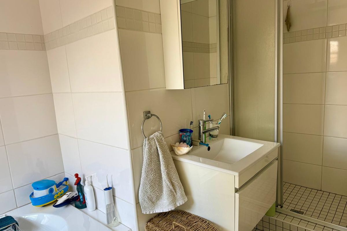 A functional bathroom featuring a vanity cabinet with integrated sink, a shower enclosure, and neutral wall tiling.
