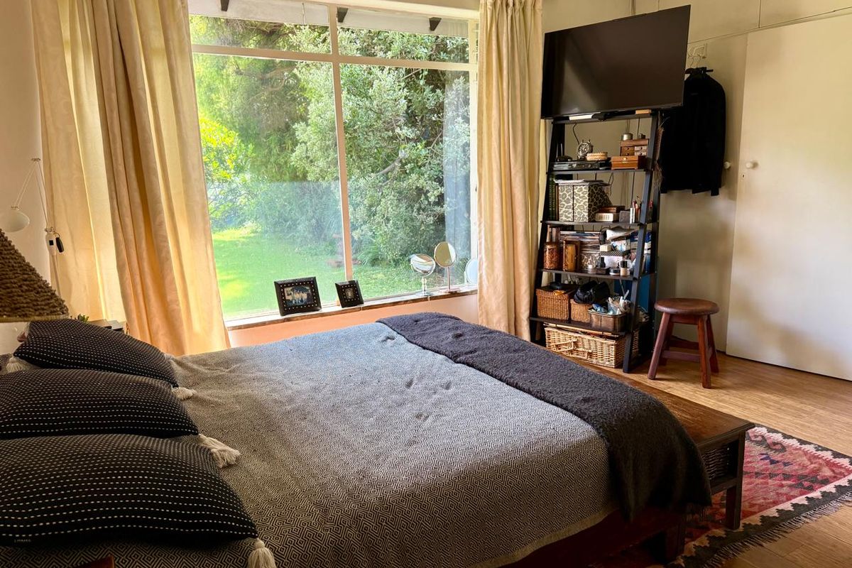 A cozy bedroom featuring large picture windows with garden views, built-in storage cupboards, and warm timber flooring.