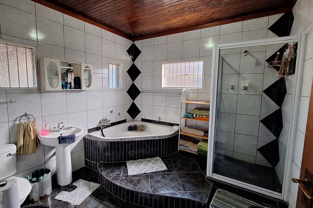 A functional bathroom featuring a corner bathtub, separate glass-enclosed shower, pedestal basin, and toilet, finished with tiled walls and a timber-paneled ceiling.