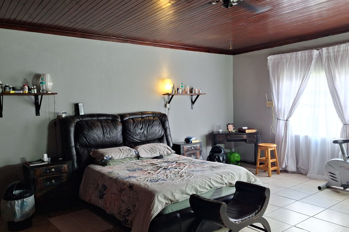 A spacious bedroom featuring tiled flooring, a timber-paneled ceiling, and large windows with curtains, providing a functional and well-lit living space.