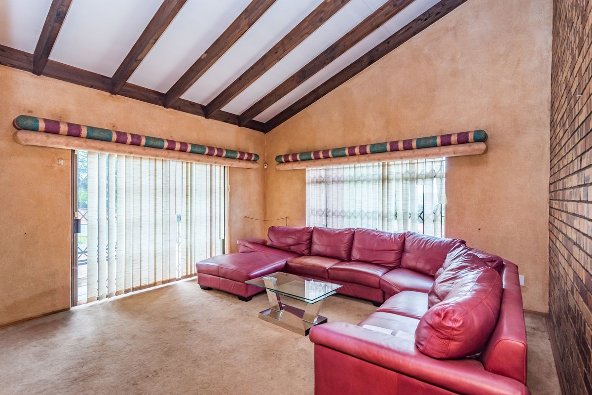 Spacious living room featuring a vaulted ceiling with exposed timber beams, a brick feature wall, and large sliding doors leading to the exterior.