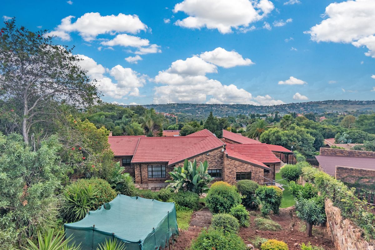 Aerial view of a brick-faced house with a tiled roof, set within a lush, established garden and surrounding neighborhood landscape.