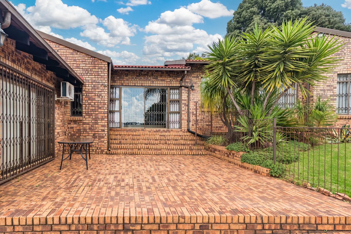 A well-maintained rear exterior featuring a spacious brick-paved patio, facebrick facade, and secure metal gates, providing a functional outdoor living space.