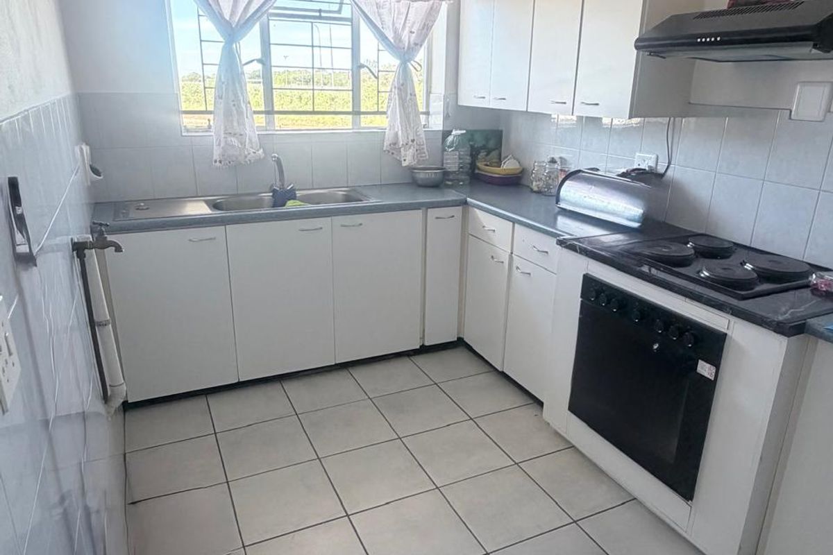 A functional kitchen featuring white cabinetry, tiled flooring, a built-in oven with hob, and a stainless steel sink under a window.