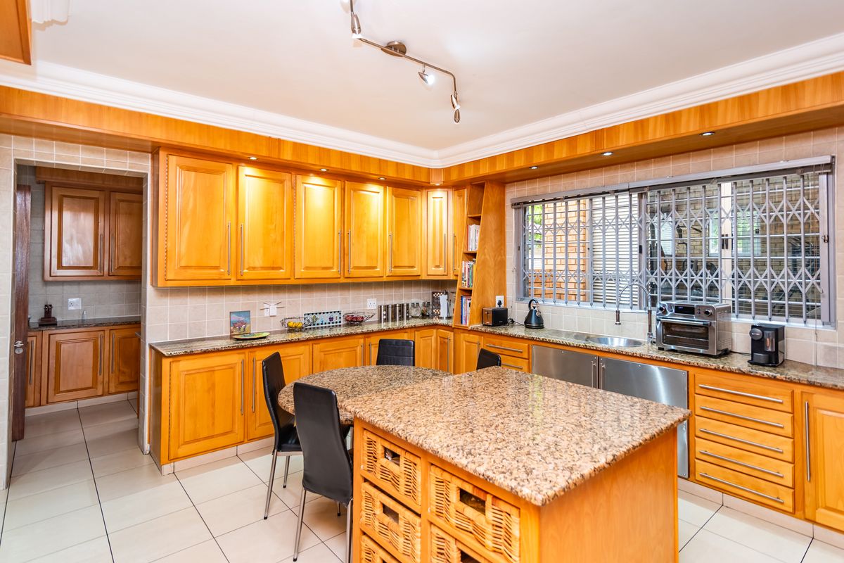 Spacious kitchen featuring warm wooden cabinetry, granite countertops, tiled flooring, and a central island, with an adjacent scullery area visible.