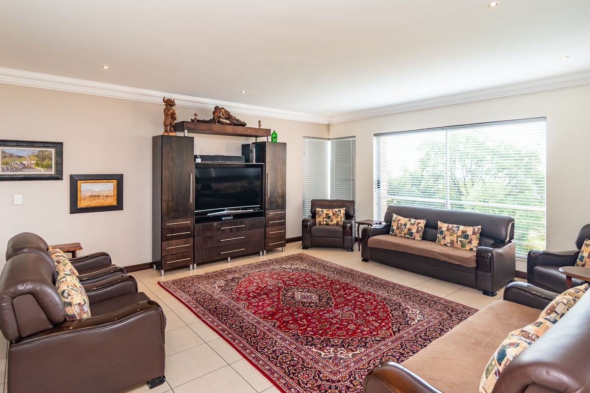 Spacious living room featuring neutral walls, tiled flooring, crown molding, and large windows with venetian blinds, offering a comfortable and well-maintained living space.