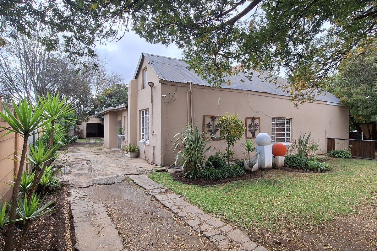 Side view of the property featuring a stone-paved driveway, established garden beds, and a corrugated metal roof.