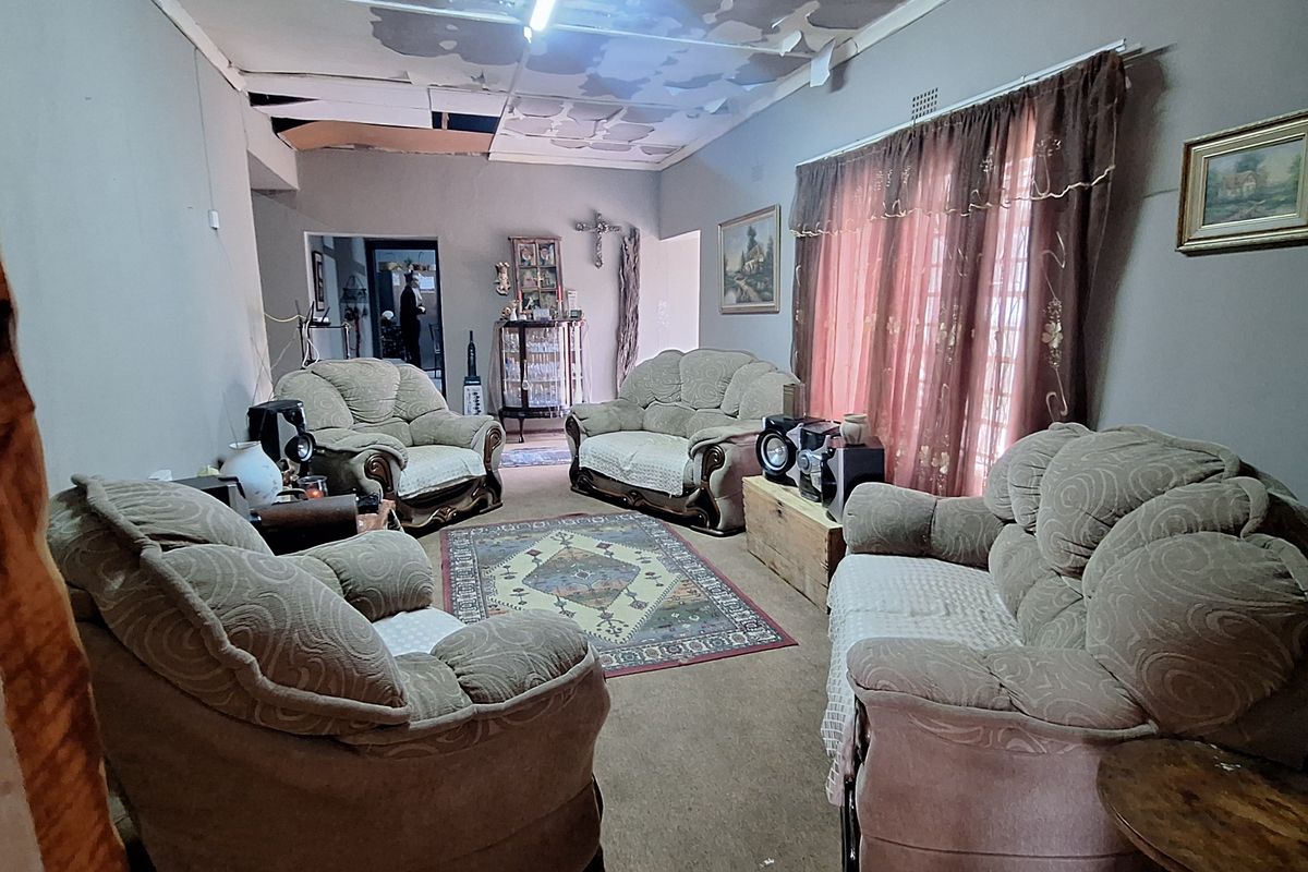 A living room featuring a significant ceiling repair requirement, carpeted flooring, and large windows with curtains.