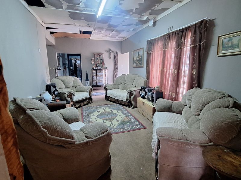 A living room featuring a significant ceiling repair requirement, carpeted flooring, and large windows with curtains.