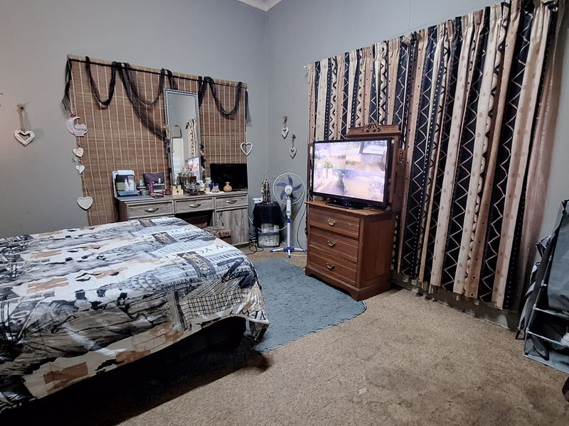 A bedroom featuring carpeted flooring, large window curtains, and visible wall cracks, offering a functional space with potential for cosmetic updates.