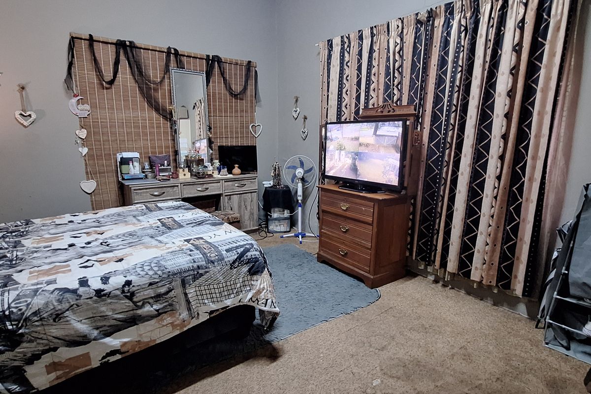A bedroom featuring carpeted flooring, large window curtains, and visible wall cracks, offering a functional space with potential for cosmetic updates.