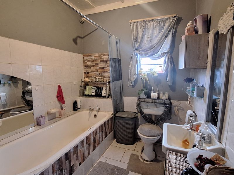 A dated bathroom featuring a built-in bathtub with tiled surround, a pedestal washbasin, and a toilet, requiring cosmetic updates and maintenance.