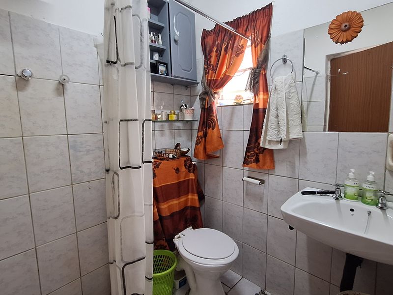 Compact bathroom featuring a wall-mounted basin, toilet, and shower area with tiled walls and built-in storage cabinetry.