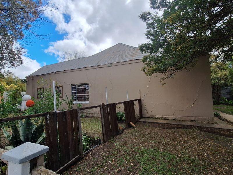 Exterior view of the property showing a side facade with visible structural wall cracks and a weathered garden fence.