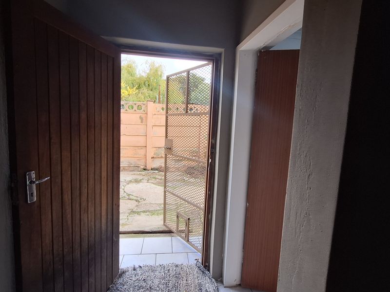 An interior view of an entryway leading out to a rear courtyard, featuring tiled flooring and a security gate.