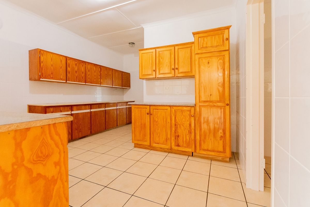 A spacious, empty kitchen featuring extensive wooden cabinetry, laminate countertops, and neutral tiled flooring, offering a functional layout ready for modernization.