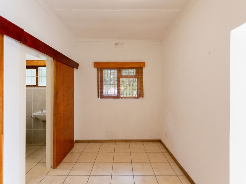 A bright, empty bedroom featuring neutral tiled flooring, a wooden sliding door, and a window with timber framing.