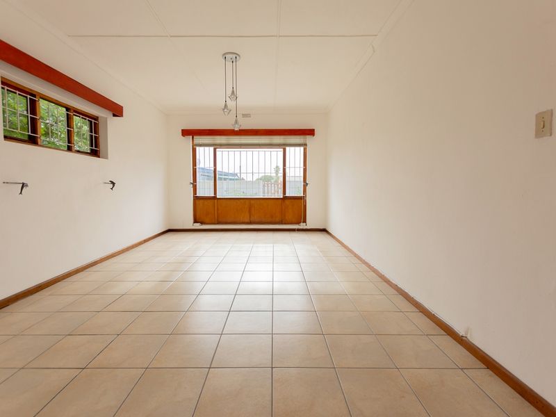 A spacious, empty living area featuring neutral ceramic tile flooring, security bars on windows, and simple pendant lighting, ready for personalization.
