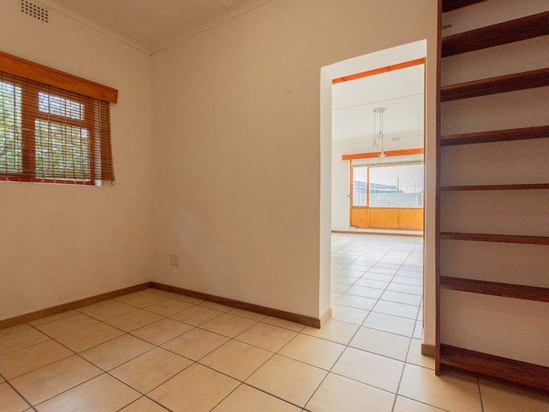 An empty bedroom featuring tiled flooring and a built-in wooden shelving unit, with a doorway leading into an adjacent living area.