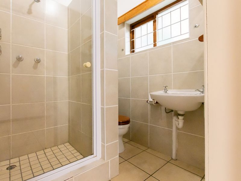 A functional bathroom featuring a tiled shower enclosure, a wall-mounted basin, and a toilet, finished with neutral wall and floor tiles.