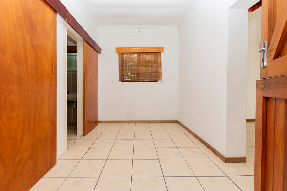 An empty bedroom featuring tiled flooring, sliding wooden doors, and a window with wooden trim, offering a blank canvas for personalization.