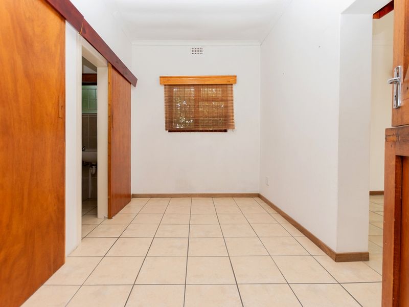 An empty bedroom featuring tiled flooring, sliding wooden doors, and a window with wooden trim, offering a blank canvas for personalization.