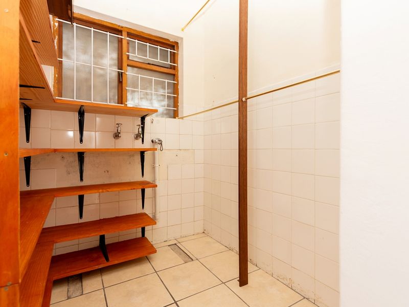 A functional laundry area featuring tiled walls and flooring, timber shelving, and existing plumbing connections, ready for modernization or utility use.