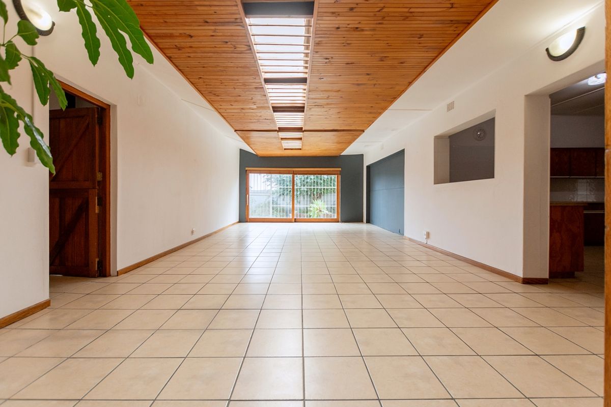Spacious, empty living area featuring a distinctive timber-clad ceiling with a central skylight, ceramic tiled flooring, and a sliding door leading to the exterior.